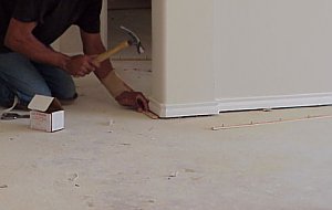 A workman installs a tackless strip. 