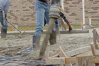 One person places concrete in the front of this picture while others level the poured concrete in the background.