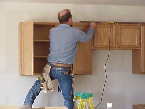 The workman makes sure that each cabinet is aligned before attaching it to the wall.